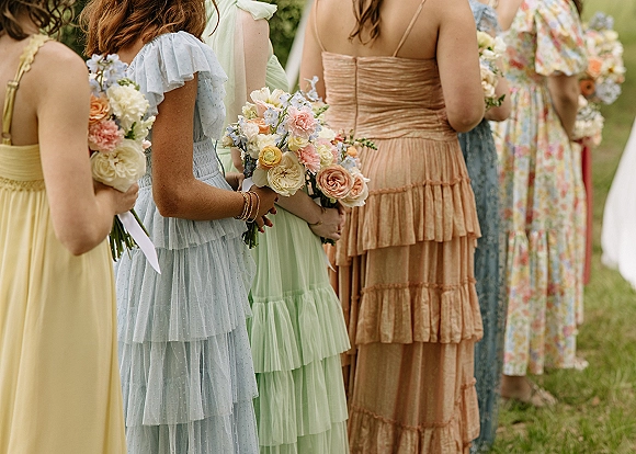 Bridesmaids bouquets held in a lineup, paired with pastel bridesmaid dresses and ribbon-wrapped rose blooms on a green outdoor lawn