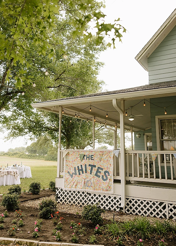 Wedding welcome sign on a handmade wedding banner with bunting flags and string lights, hanging on a farmhouse porch above lawn tables