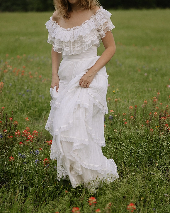 Wedding dress with an off the shoulder neckline and ruffle lace bodice, tiered skirt and lace trim, shown in a wildflower meadow