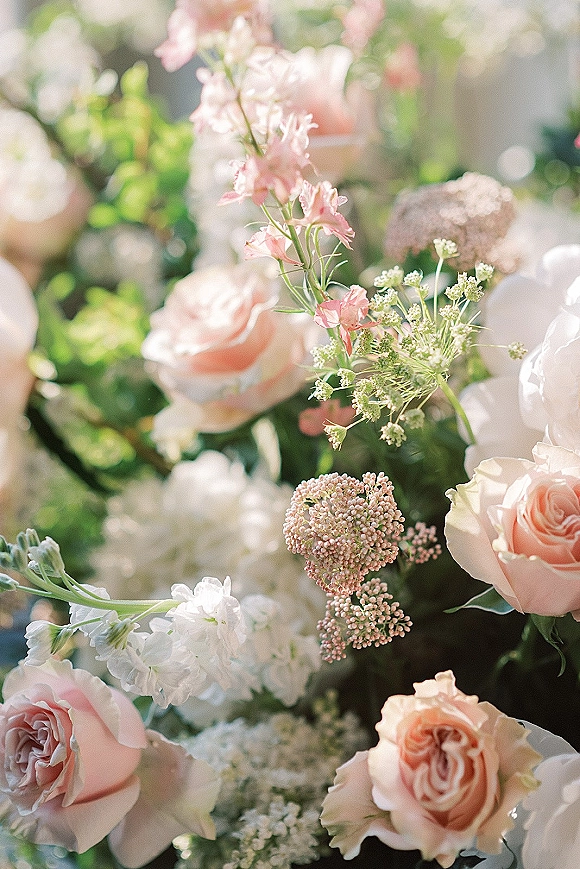 Wedding flowers with blush rose centerpiece, white blooms and greenery, softly lit in natural light with dreamy bokeh background