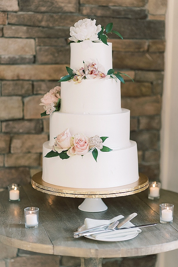 Wedding cake four tier wedding cake with blush roses, peony and orchid accents on a gold stand, styled with votive candles by a stone wall