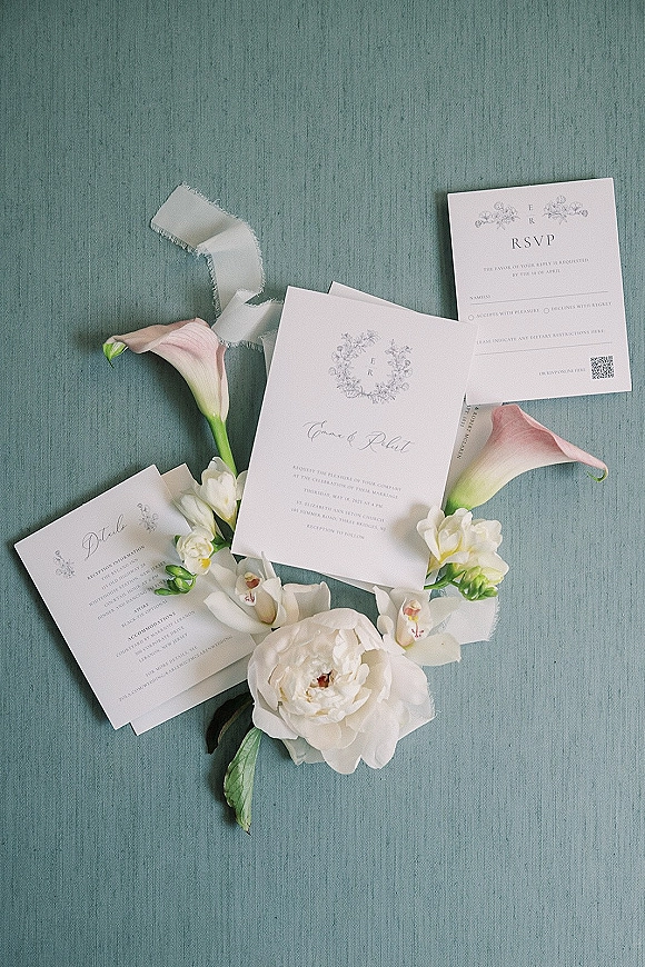 Invitation suite wedding invitation flat lay with RSVP and details cards tied in vellum ribbon, styled with calla lilies on blue linen backdrop