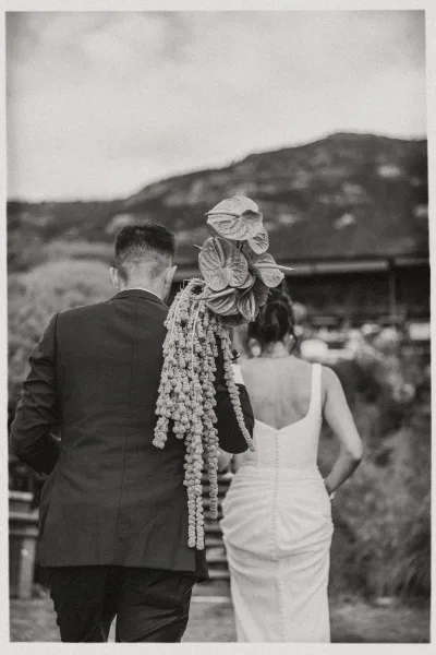 Couple portrait in black and white, bride and groom walking away on a mountain path, groom holding a cascading anthurium bouquet