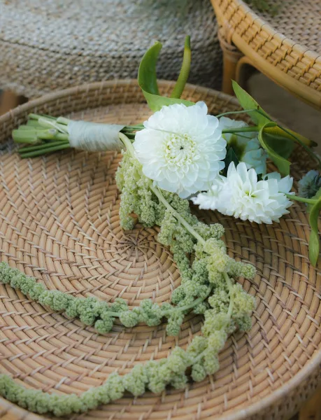 Wedding bouquet with white dahlia blooms and cascading green amaranthus, ribbon-wrapped, resting on a woven rattan chair flatlay