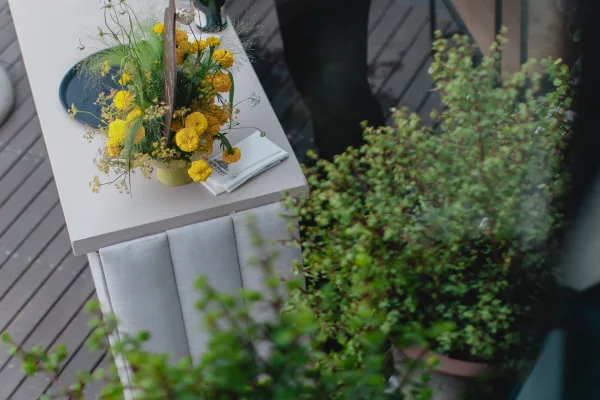 Wedding welcome table with a wedding welcome sign beside yellow flowers in a ceramic vase, printed programs, on a wood deck patio
