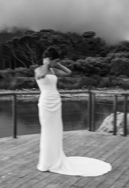 Bridal portrait of a bride in a strapless wedding dress with a long train on a lakeside wooden deck under a cloudy sky