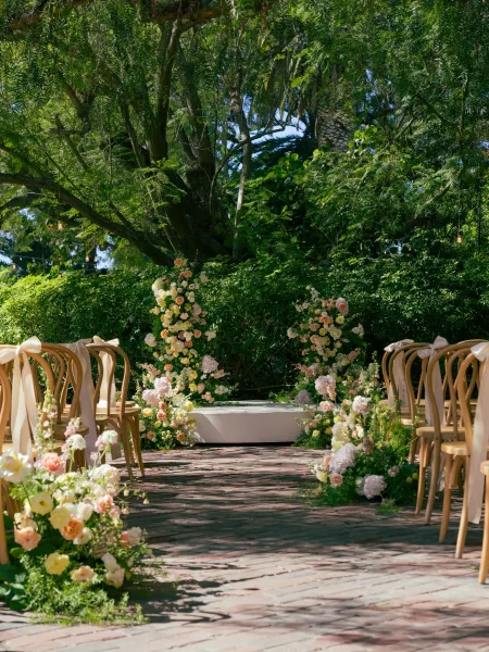 Ceremony aisle decor with outdoor ceremony aisle flowers, pastel ground florals lining a brick walkway to a platform under string lights in a garden