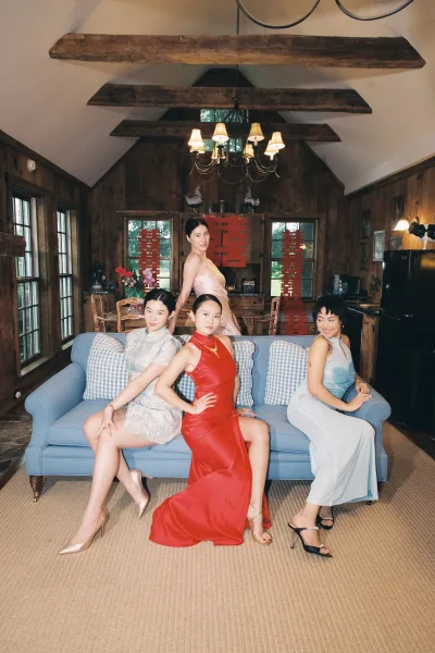 Bridesmaid portrait of women on a couch in formal satin and cheongsam gowns, one in red, beneath a chandelier in a rustic cabin interior