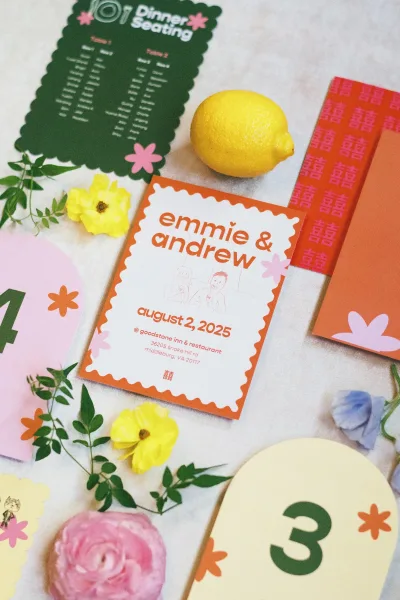 Wedding invitation suite with colorful wedding invitations, red patterned envelope liner, table number cards, lemon and flowers on white fabric backdrop