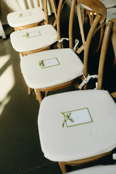 Ceremony seating arranged with refined ceremony chair decor on wood crossback chairs, each holding wedding programs for guests.