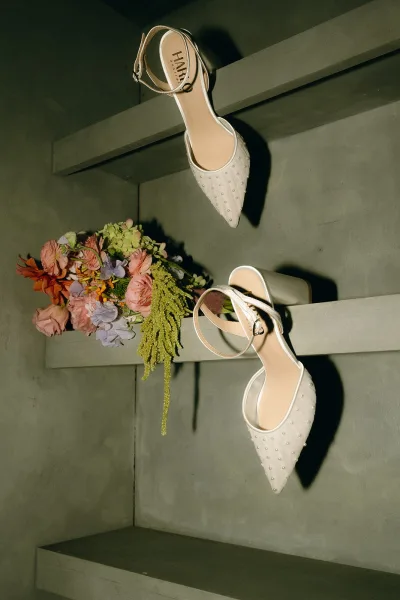 Bridal shoes, pearl wedding heels arranged beside a bouquet, their elegant lines and soft sheen creating a gentle, romantic mood.