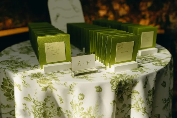 Escort card display with green escort cards arranged on a wood ledge, organized by an alphabet divider sign against garden greenery.