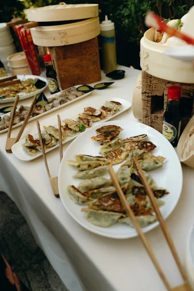 Dumpling station at a wedding food station, bamboo steamers brimming with bites, set against lush garden greenery.