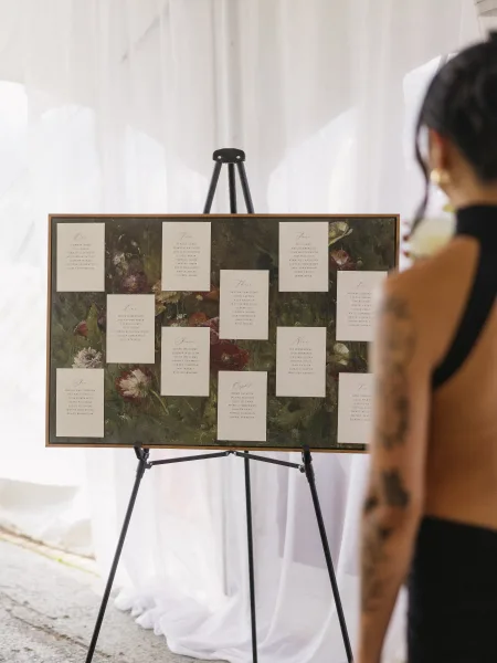 Wedding seating chart featuring floral artwork in a classic serif design, set inside a white-draped tented reception.