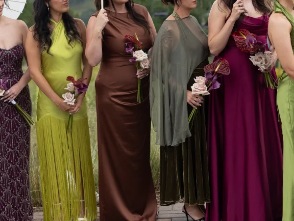 Bridesmaid dresses styled as mismatched bridesmaid dresses in jewel tones gather beneath a parasol on a brick garden path