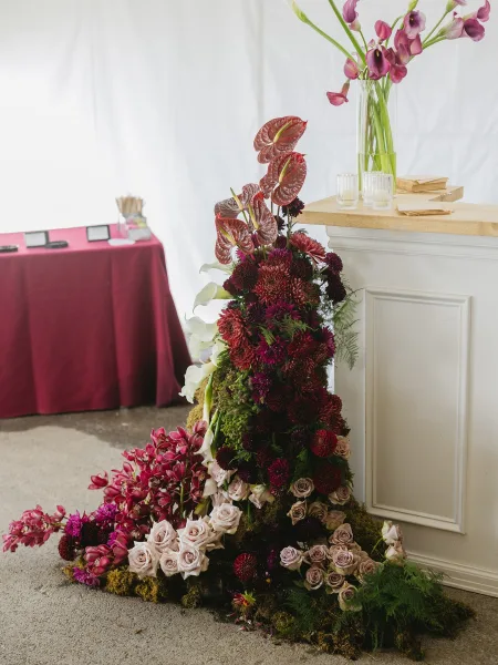Bar floral arrangement of wedding bar flowers with sculptural orchids, framed by white drapery and a burgundy tablecloth.