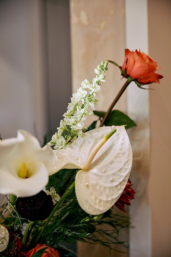 Wedding floral arrangement with calla lily wedding flowers, anthurium, orange roses, white stock, greenery, and pearl accents by doorway trim