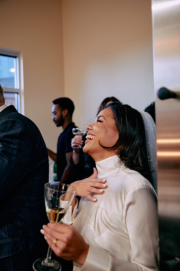 Bride portrait of a bride laughing candid while holding a champagne flute, veil draped over a high neck dress at an indoor reception