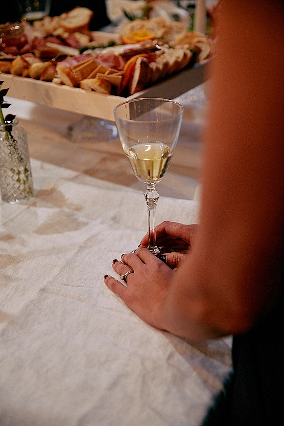 Wedding reception table with a wedding charcuterie board, wine glass, and candle on linen, with blurred guests in the background