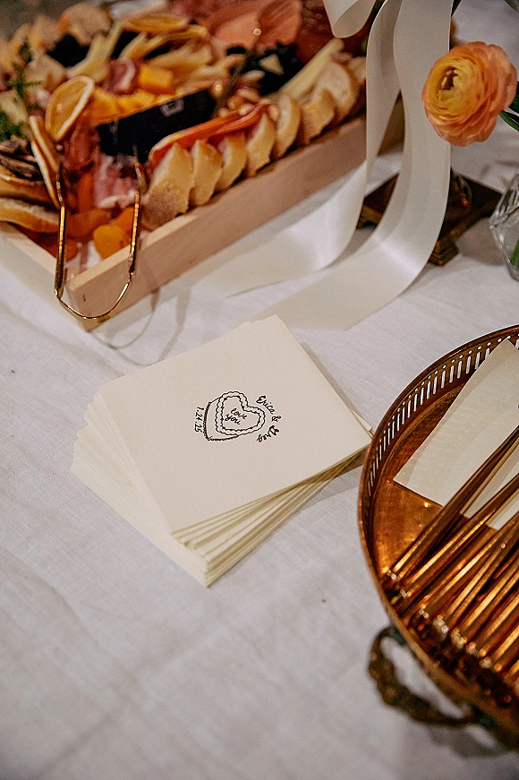 Wedding cocktail napkins with personalized cocktail napkins heart monogram tied with ribbon on a charcuterie board on a white linen tablecloth
