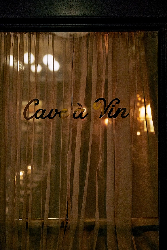 Wedding venue sign with black script window lettering on glass, framed by sheer curtains and warm interior lights in the background