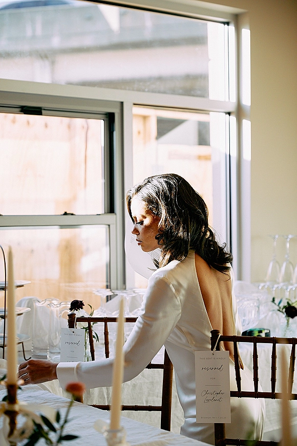 Reception tablescape with modern wedding tablescape styling, taper candles, calligraphy place cards, bud vases and greenery by large windows in daylight