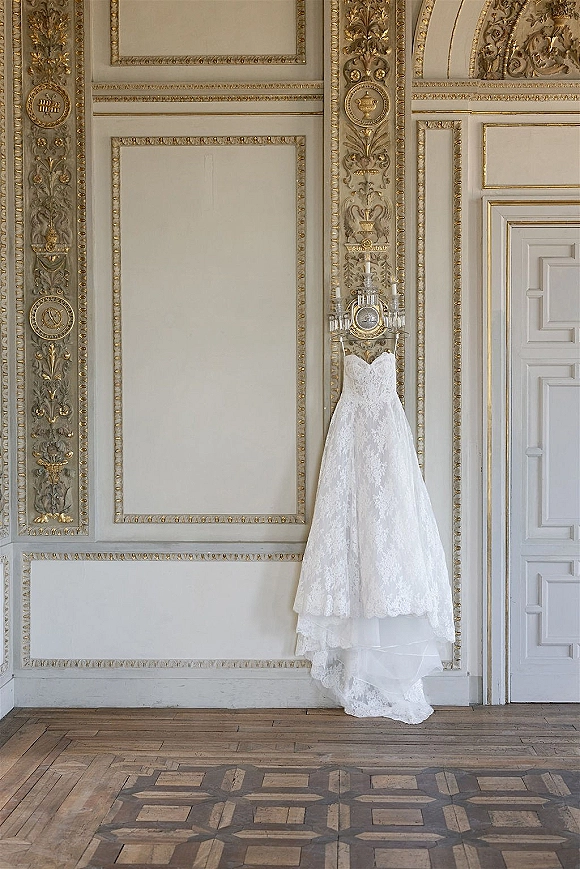 Wedding dress, lace wedding dress hanging from a chandelier with sheer lace overlay and strapless sweetheart neckline in an ornate paneled room