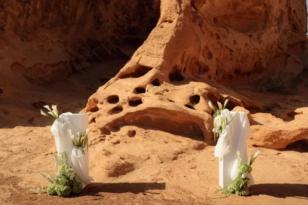 Ceremony aisle decor with calla lily floral clusters on white pedestals and draped fabric, set against a red rock canyon backdrop