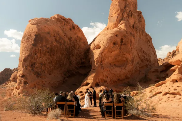 Outdoor wedding ceremony in the desert with bride and groom at the aisle as guests sit on wooden chairs beneath red rock formations