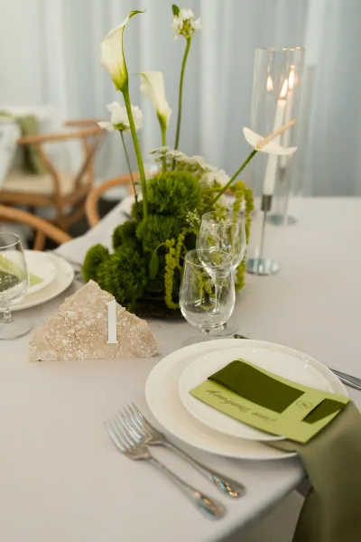 Reception tablescape with wedding table centerpiece of white calla lilies and greenery, taper candles, menus, and glass hurricane candle holder