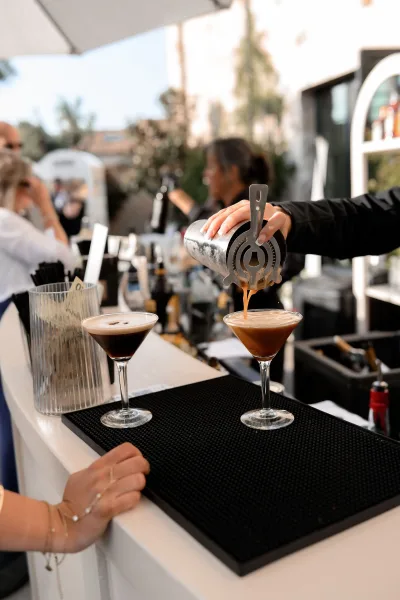 Espresso martini, the wedding signature drink, with a coffee bean garnish at an outdoor bar amid garden trees and a patio umbrella.