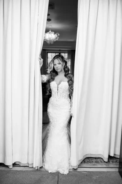Bridal portrait of a bride in doorway, wearing an elegant long-sleeve gown beneath a glowing chandelier.
