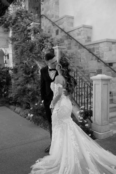 Wedding kiss portrait as the bride and groom kiss on a stone staircase, her long train sweeping beside wrought iron railings and vines.