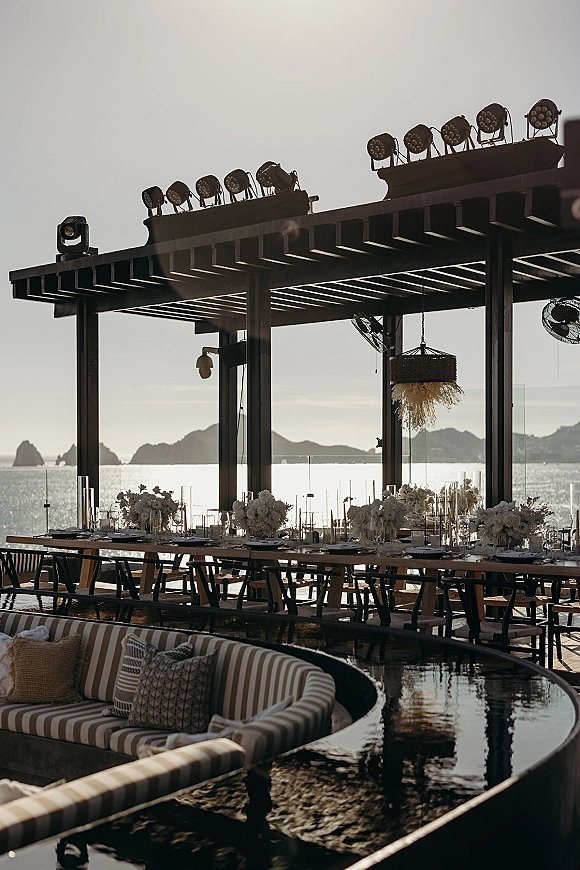 Reception tablescape with outdoor reception tablescape styling on a long banquet table, candlelit florals under a pergola at sunset ocean view