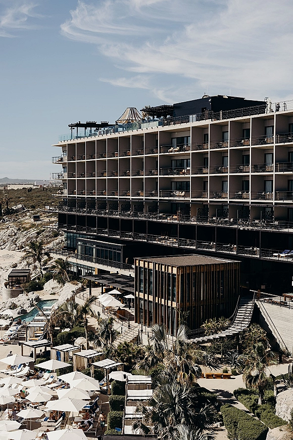 Wedding venue exterior of a modern wedding venue with glass balconies, poolside cabanas and palms, set on a coastal hillside under blue skies