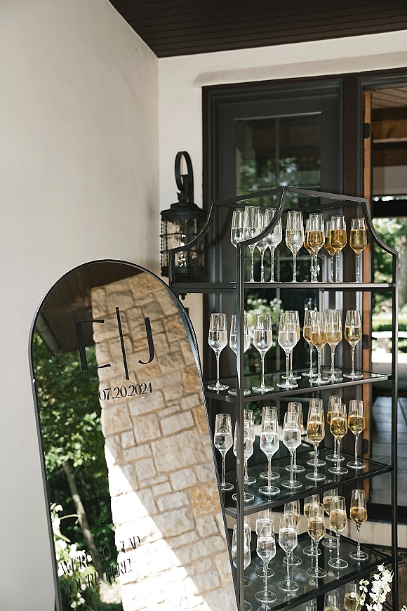 Champagne tower setup with wedding champagne tower flutes on a black metal stand beside an acrylic sign on a patio porch by greenery