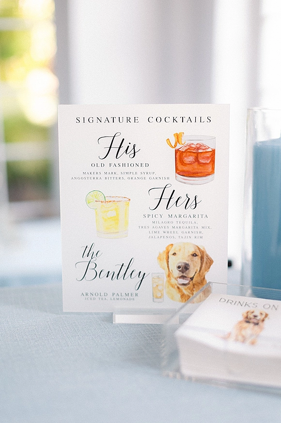Signature cocktail sign displaying wedding signature cocktails with illustrated drink icons and dog accent on a linen table by greenery window light
