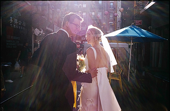 Couple portrait of bride and groom walking on a city street wedding photo, bride looking back in veil holding bouquet under string lights
