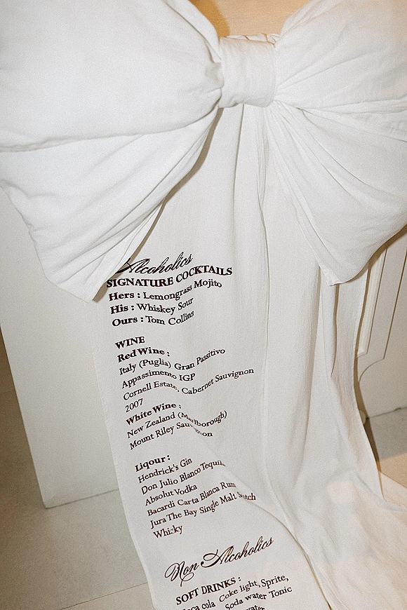 Bar menu sign with a white bow on an easel, featuring a wedding bar menu printed in clean typography against an indoor wall