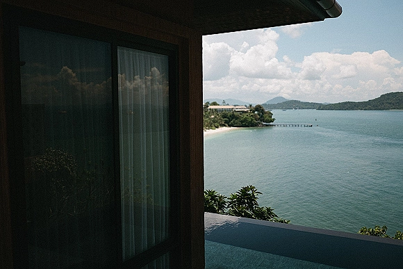 Ocean view balcony at a wedding venue with wood wall, glass window and curtains, overlooking islands, coastline, pier and clouds