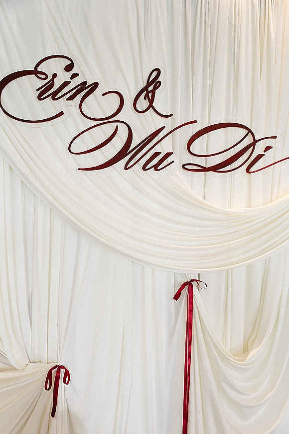 Wedding backdrop with draped fabric backdrop, flowing white curtain panels and calligraphy lettering, finished with satin ribbons