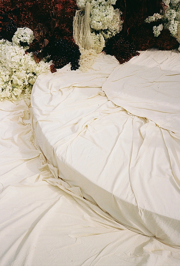 Wedding cake with draped wedding cake frosting, tiered in white buttercream with hydrangeas and dark grapes against a moody floral backdrop