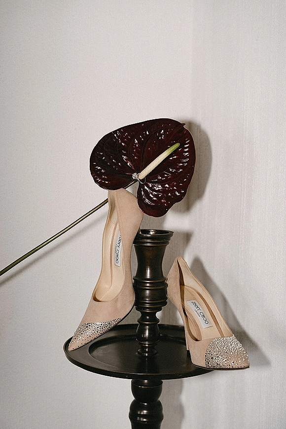 Bridal shoes in nude wedding heels with rhinestone sparkle on a black pedestal, paired with anthurium flower against a white wall