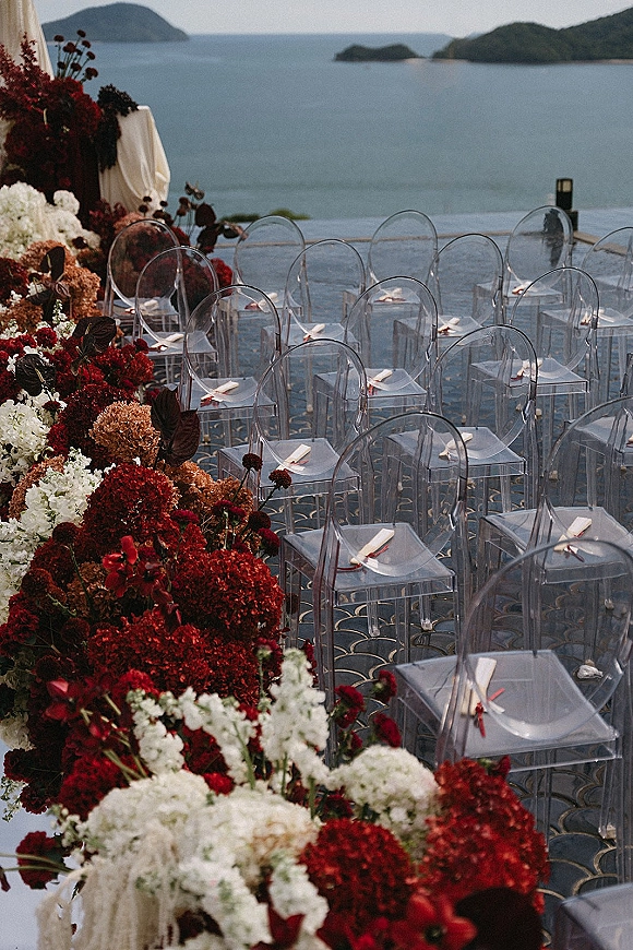 Ceremony setup with outdoor wedding ceremony details, clear acrylic chairs, hydrangea-lined aisle petals, and draped fabric on an ocean-view terrace