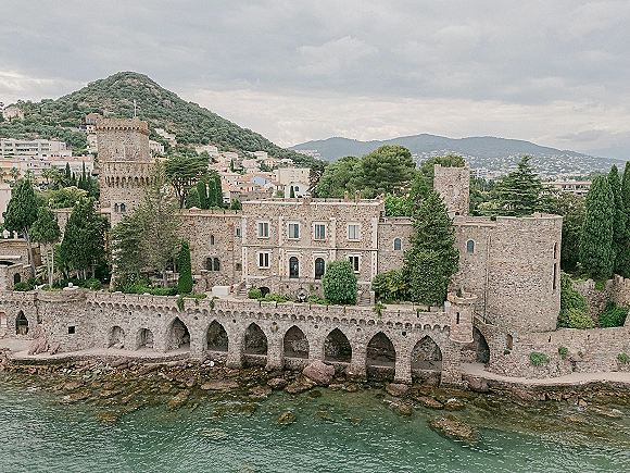 Castle wedding venue with a stone castle accent, towers and arched seawall overlooking a rocky ocean shoreline under cloudy skies
