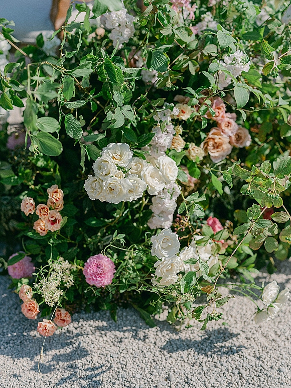 Wedding floral arrangement with ceremony ground florals of garden roses, pink blooms, and airy greenery on gravel ground
