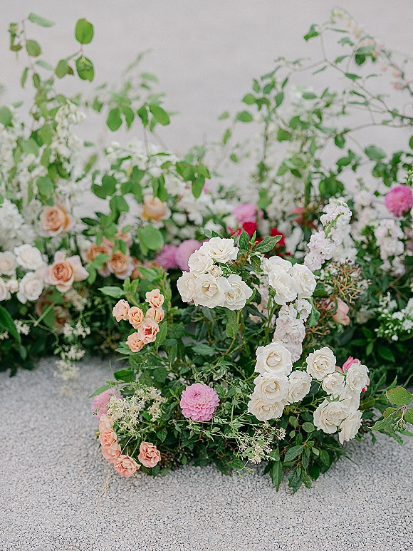Wedding floral arrangement ground floral installation of roses and greenery foliage with flowering branches on gravel against a white wall