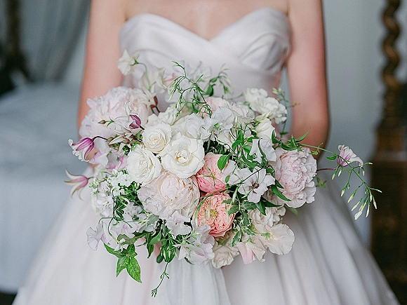Bridal bouquet of white and blush bouquet blooms with peonies, white roses and greenery held against a strapless gown by an ornate mirror frame