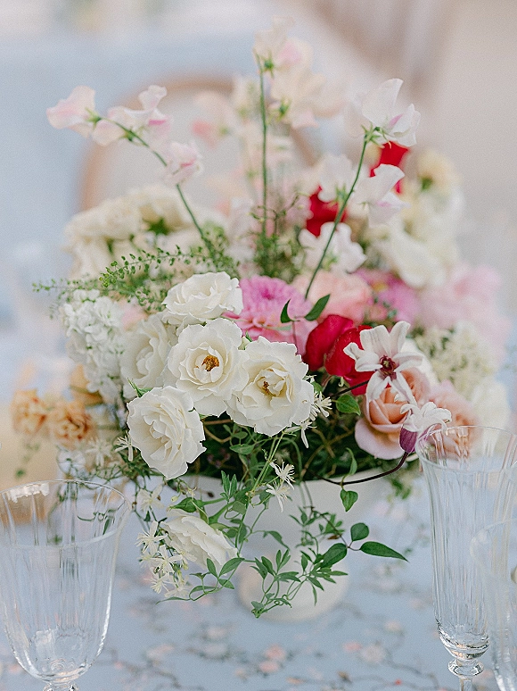 Wedding centerpiece with white roses and pink blooms in a bud vase, accented by crystal champagne flutes and petals on a reception table