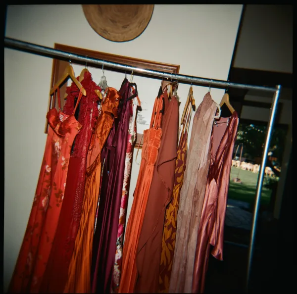 Bridesmaid dresses in a bridesmaid dress color palette hanging on a rack, featuring satin, lace, and floral prints by a window